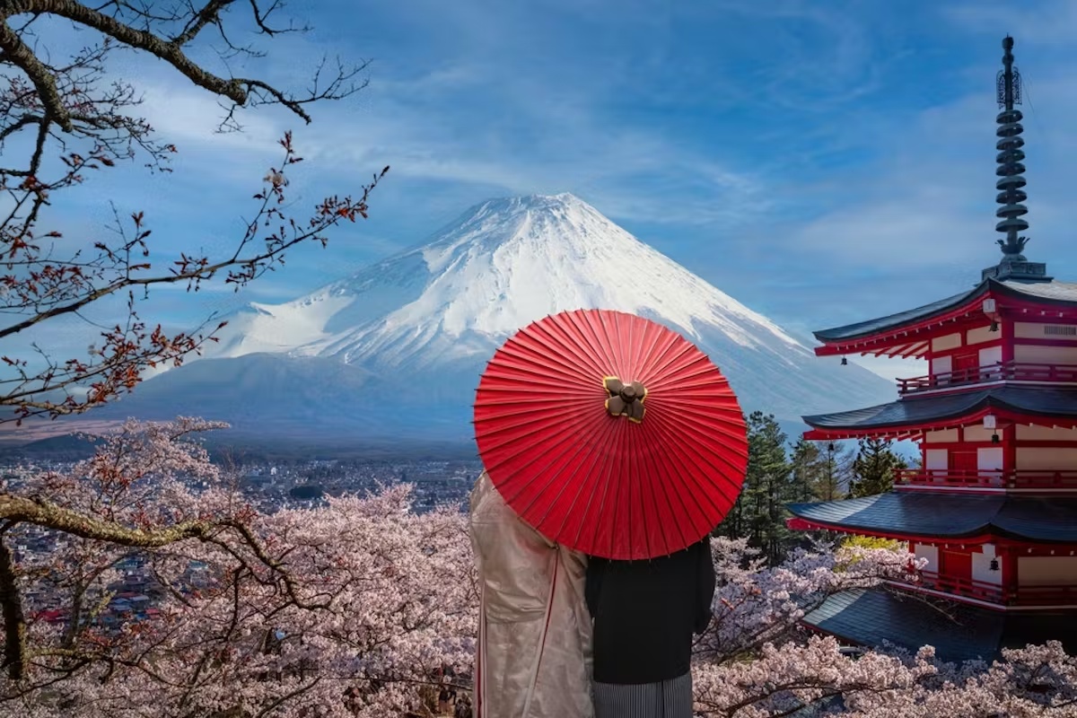 Mount Fuji, cherry blossoms, and a red pagoda with travelers beneath a red parasol