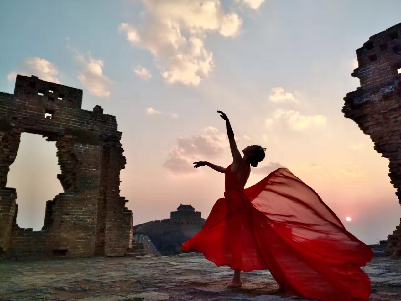 A dancer in a flowing red dress on the Great Wall at sunset