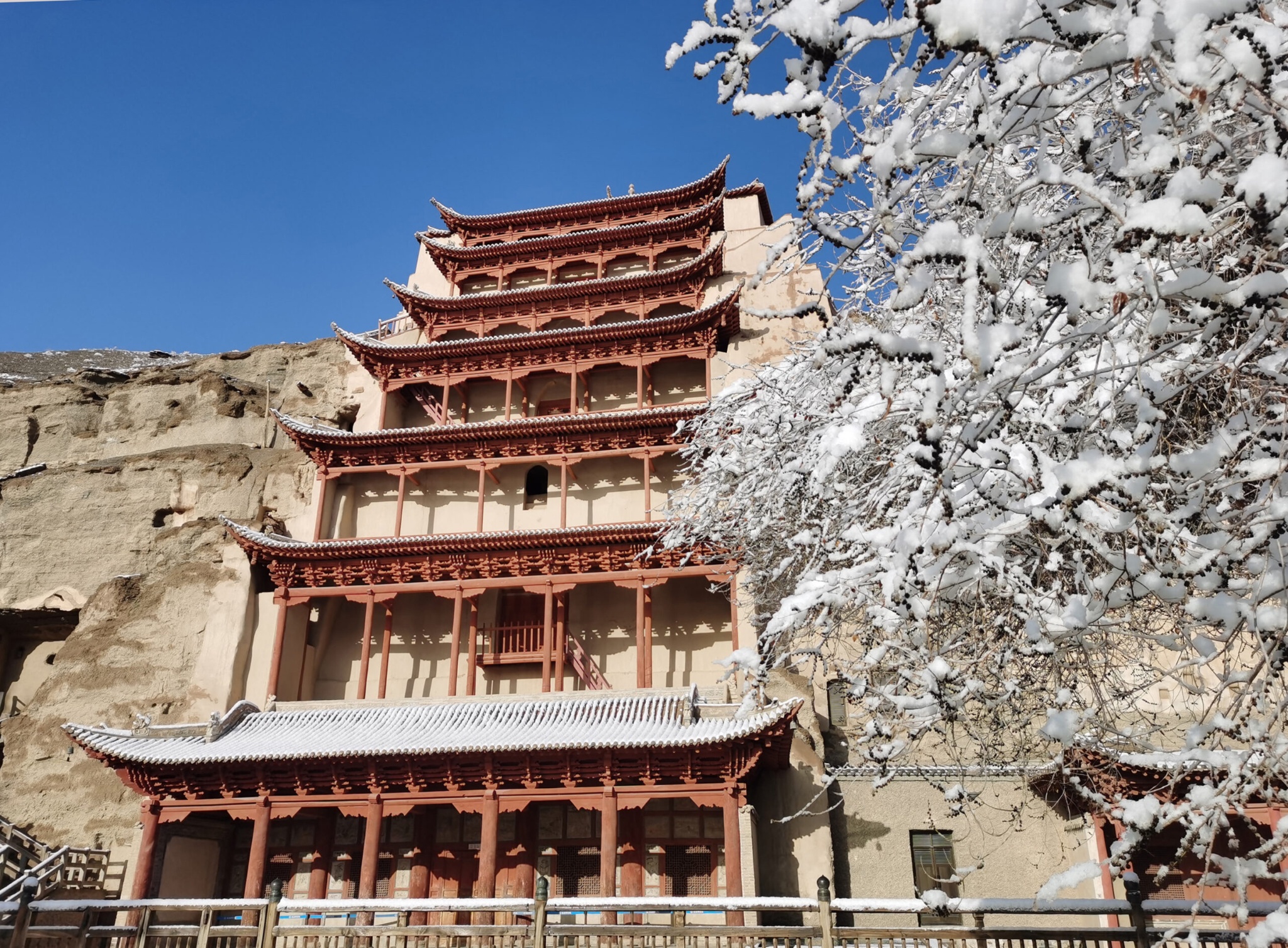Traditional multistory temple facade beside snow-covered trees and a rocky cliff