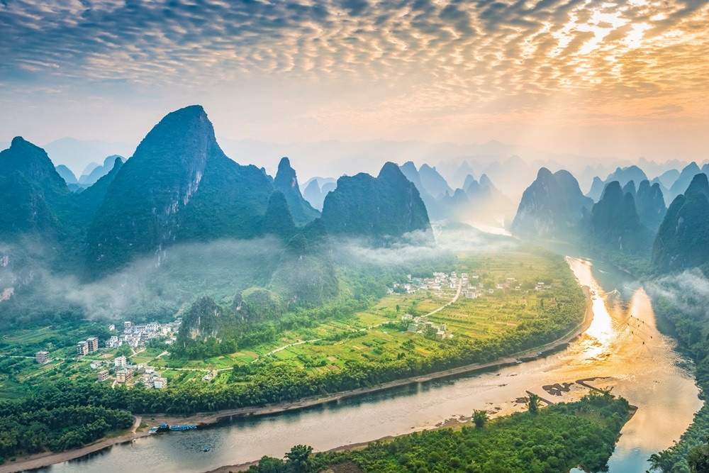 Winding river and limestone mountains above green fields and villages in golden light