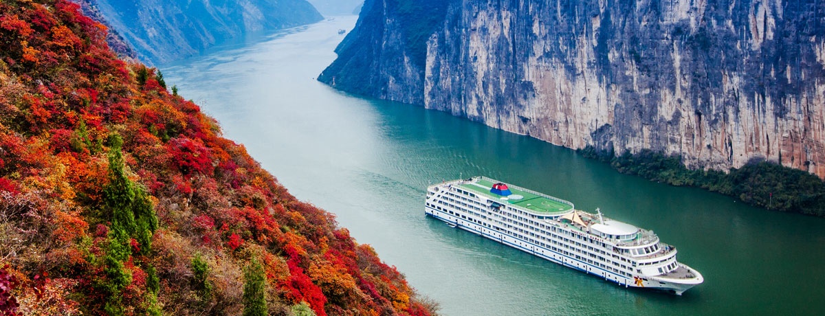 Cruise ship sailing through the Three Gorges beside autumn-colored mountains